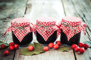 Three jars of jam and hawthorn berries on rustic table clipart
