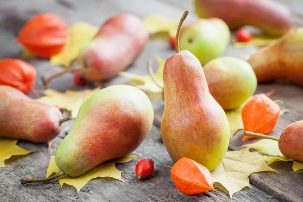 Ripe pears on wooden table with autumn leaves and berries. — Stock Photo, Image