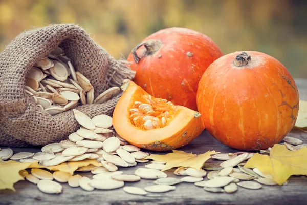 Calabazas y bolsa de lona con semillas de calabazas en mesa de madera . — Foto de Stock