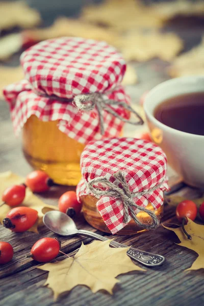 Frascos de miel y taza de té. Hojas de arce y bayas de perro — Foto de Stock