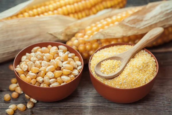 Corn grits and seeds in bowls, corncobs on kitchen table. — Stock Photo, Image