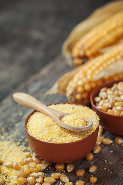 Corn groats and seeds in bowls, corncobs on background. — Stock Photo, Image