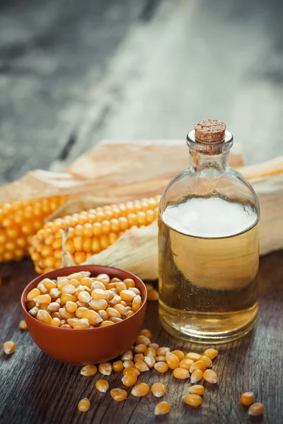 Botella de aceite esencial de maíz, semillas en tazón y dos mazorcas de maíz — Foto de Stock