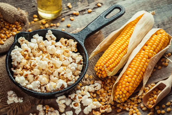 Palomitas preparadas en sartén, semillas de maíz en tazón y mazorcas de maíz — Foto de Stock