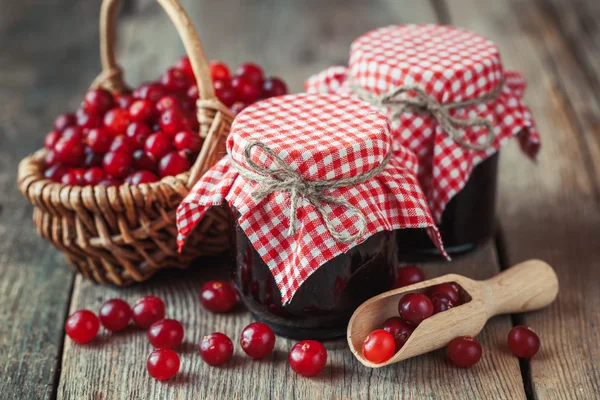 Potten van Amerikaanse veenbessen jam en mand met moeras berry op achtergrond. — Stockfoto