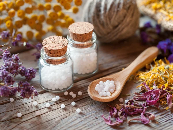 Flaschen mit homöopathischen Globuli, Löffel und trockenen gesunden Kräutern — Stockfoto