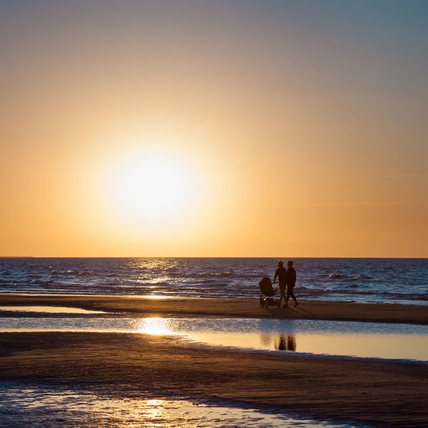 Deniz günbatımı ve bebek carriag ile aile çiftin siluetleri — Stok fotoğraf