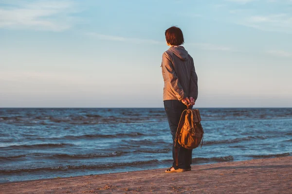 Menina turística com mochila olhando para o mar ao pôr do sol . — Fotografia de Stock