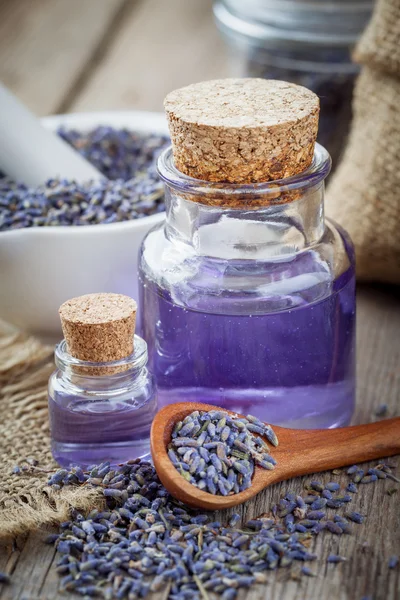 Bottles of essential oil, wooden spoon with dry lavender flowers — Stock Photo, Image