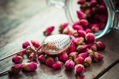 Gül tomurcukları, çay süzgeci ve rustik ahşap masa üzerinde Cam Kavanoz.