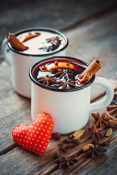 Vino caliente en tazas rústicas con especias y corazón rojo — Foto de Stock