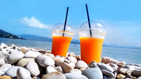 Due Bicchieri Plastica Con Succo Arancia Spiaggia Soleggiato Paesaggio Marino — Foto Stock