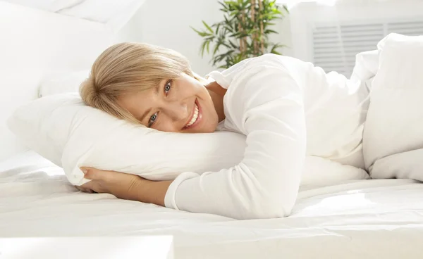 Schönes Mädchen in einem weißen Bett am Morgen, lächelnd Stockfoto