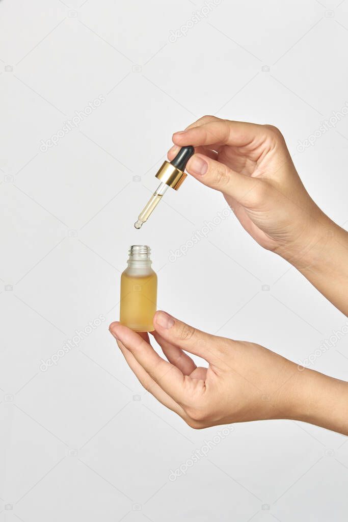 Female's hands hold a small bottle and pipet of natural medical cannabis essential CBD oil against a light grey background, copy space. Use of cannabis for medical purposes.
