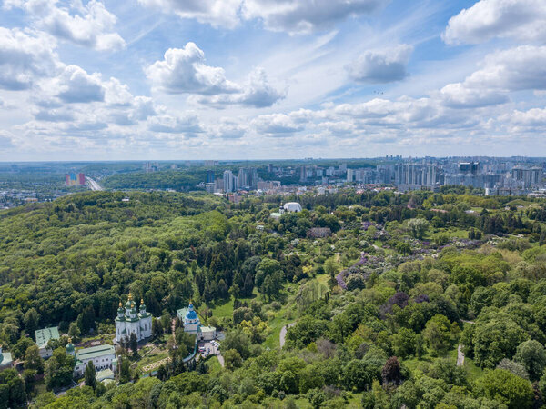 Aerial view of beautiful green botanical garden in summer, church and city buildings on horizon