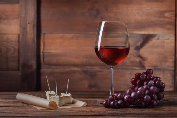 Vin rouge en verre avec raisin et fromage sur bois — Photo