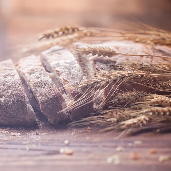 Bread and wheat on wooden table, shallow DOF — Stock Photo, Image