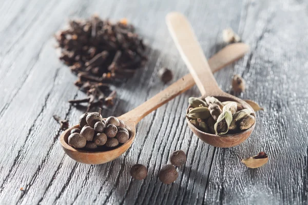 Nutmeg, clove and allspice in old spoon on wooden table — Stock Photo, Image