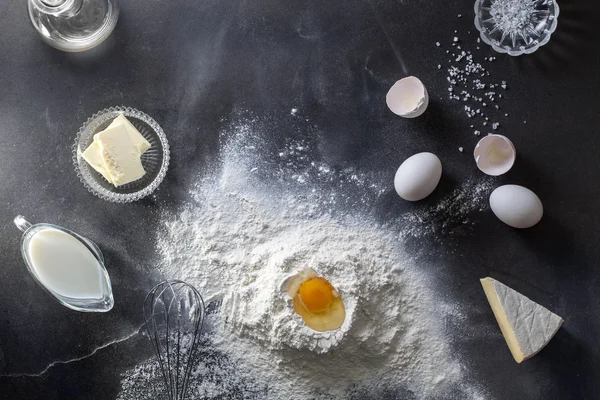Тесто на черном столе с мукой и ингридиентами — стоковое фото