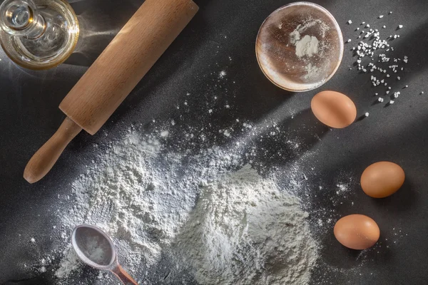 Flour and ingredients on black table — Stock Photo, Image