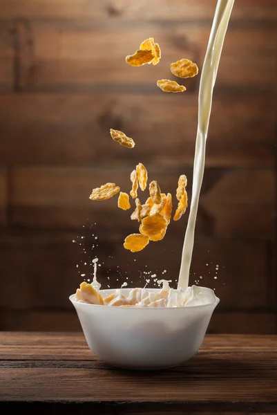 Caída de copos de maíz con salpicaduras de leche en la madera — Foto de Stock