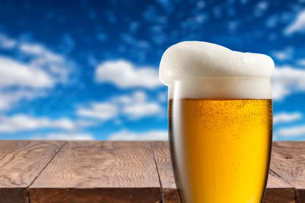 Cerveza en vidrio sobre mesa de madera contra cielo azul — Foto de Stock