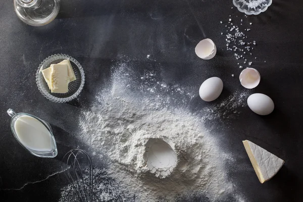 Dough on black table with flour and ingredients — Stock Photo, Image