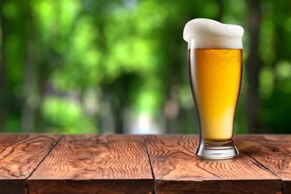 Cerveja em vidro na mesa de madeira contra verde — Fotografia de Stock