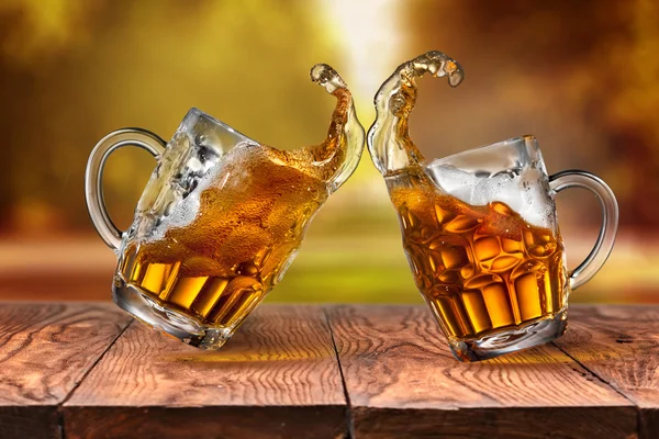 Beer in glasses with splash on wooden table against autumn leave — Stock Photo, Image