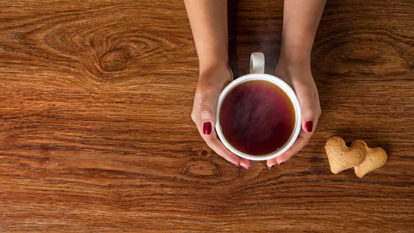 Mujer sosteniendo taza de té caliente con galletas —  Fotos de Stock