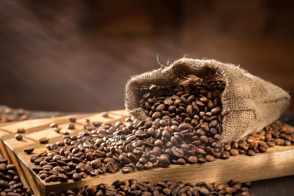 Utspillt kaffe bönor i påse på trä — Stockfoto