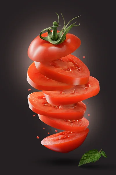 Geschnittene fliegende Tomate mit grünem Blatt auf schwarz — Stockfoto