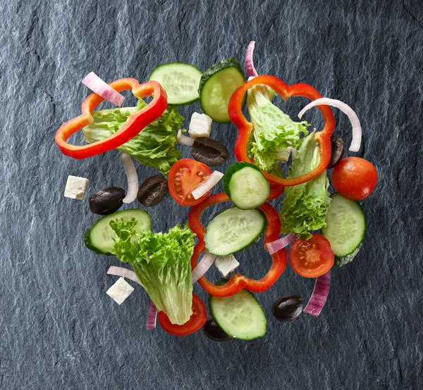 Ensalada voladora sobre fondo de pizarra — Foto de Stock