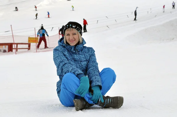 Kvinnen i vinterklær sitter på snø mot skibakken a – stockfoto