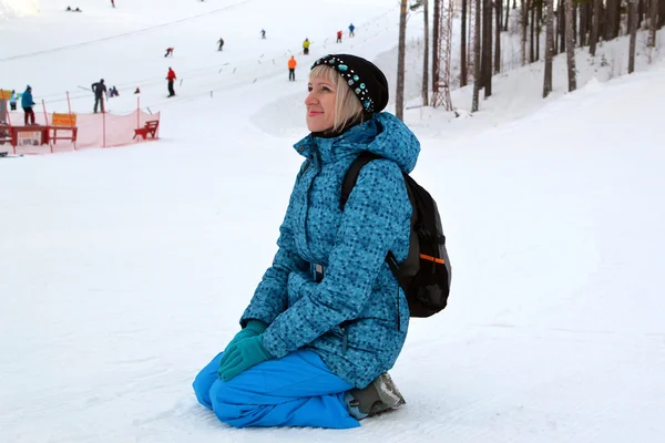 Kvinnen i vinterklær sitter på snø mot skibakken. . – stockfoto