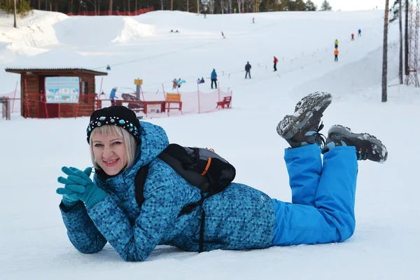 Kvinnan i vinterkläder ligger på snön mot skidbacken en — Stockfoto