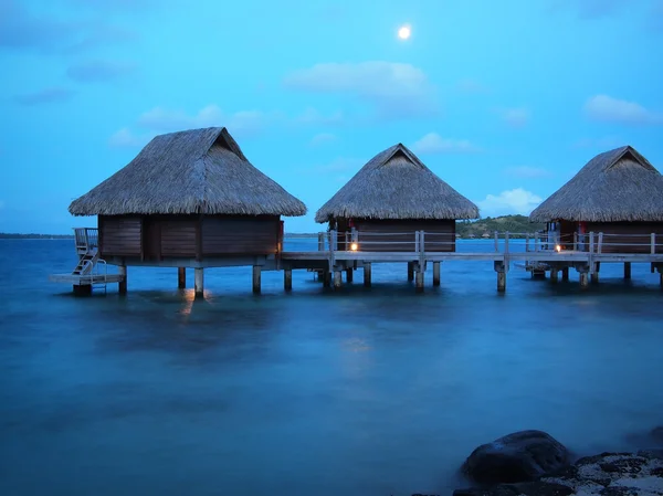 Techo de paja bungalows sobre el agua a la hora azul —  Fotos de Stock