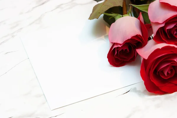 Rosas e uma folha de papel em branco sobre uma superfície de mármore — Fotografia de Stock