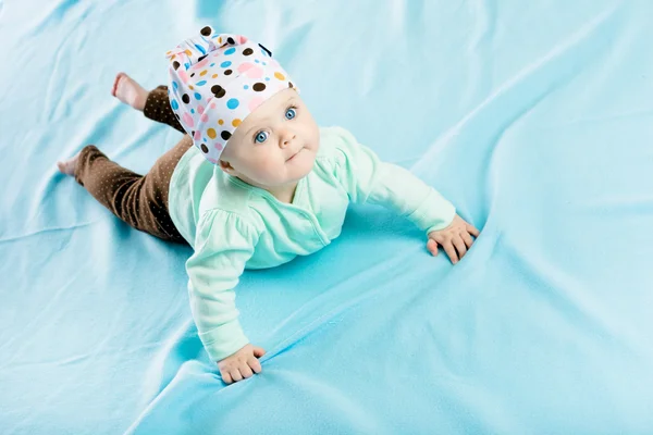 Baby in hat crawling on the blue coverlet — Stock Photo, Image