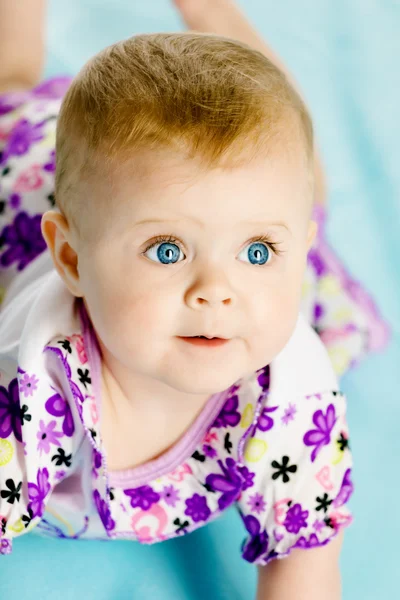 Baby girl in a dress creeps on the blue coverlet — Stock Photo, Image