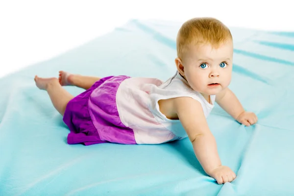 Baby girl in a dress creeps on the blue coverlet — Stock Photo, Image