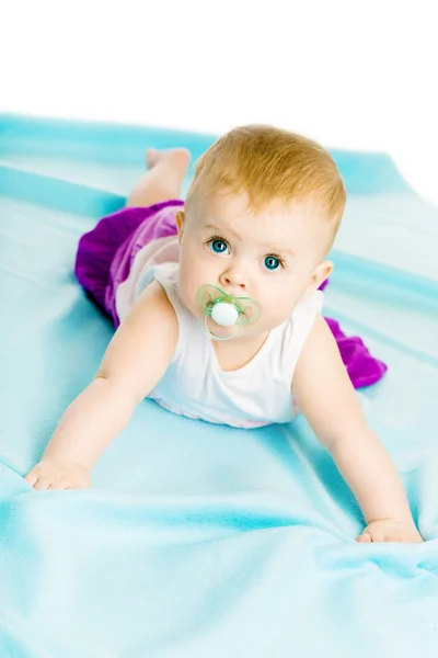 Babymeisje met fopspeen kruipen op de blauwe coverlet — Stockfoto