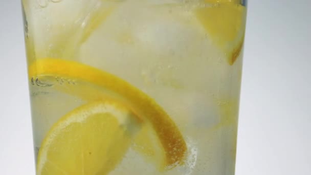 Rotující sklo ledové šumivé vody a citrónové plátky detailní up — Stock video