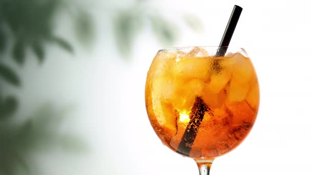 Vidro de aperol spritz cocktail com gelo e palha girando sobre desfocado folhas fundo — Vídeo de Stock