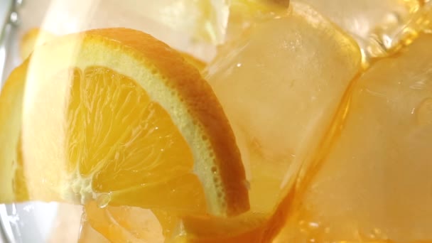 Jiskřivý nealkoholický nápoj nalévající se do sklenice pomerančových plátků a ledu, detailní zpomalený záběr — Stock video