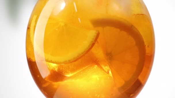 Câmera lenta perto de virar laranja aperol spritz coquetel de vidro com cubos de gelo e fatias de frutas — Vídeo de Stock