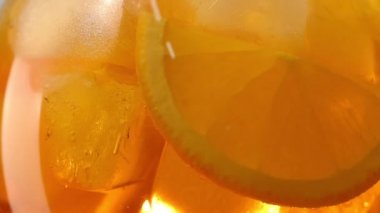 Yavaş çekimde buz küpleri ve meyve dilimleriyle portakallı aperol spreyini kokteyl bardağına çevirin.