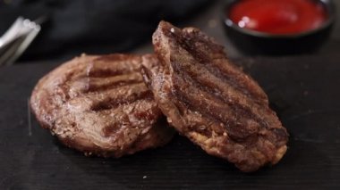 Taze ızgara bifteğin üzerine tuz düşüyor. Siyah taştan bir restoran tabağında biftek.