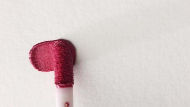 Ροζ καλλυντικό lip gloss επίχρισμα παράδειγμα εφαρμόζεται σε λευκό φόντο με ένα πινέλο απλικατέρ κοντά — Αρχείο Βίντεο