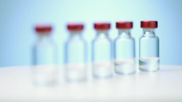 Gros plan de la ligne des flacons de vaccin médical sur fond bleu mise au point passer de la dernière bouteille à la première — Video